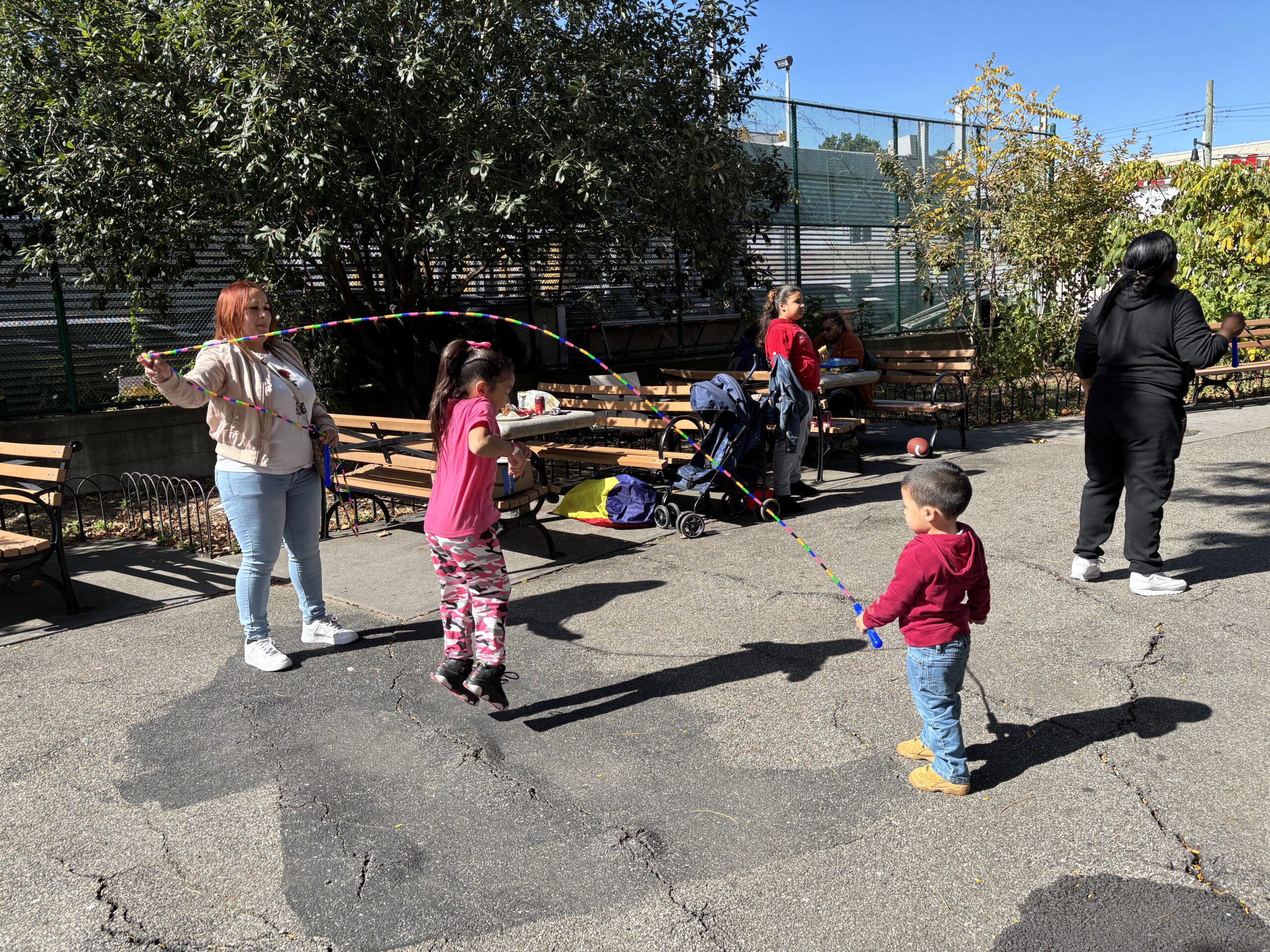 A child in pink jumps rope with her mother and brother