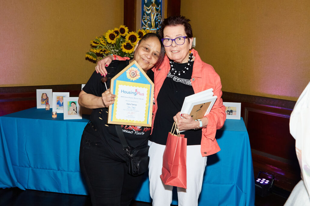 Two women with arms around one another both holding frames