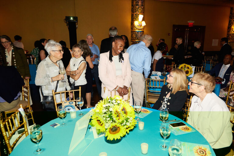 A group of people seated at a table and someone standing and speaking with them.