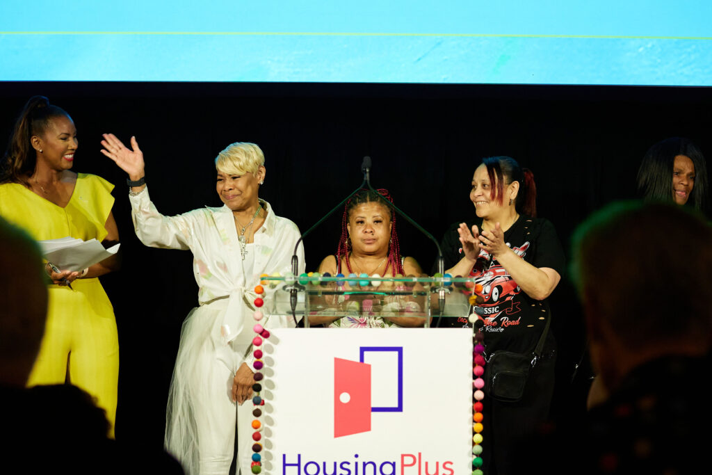 Three women stand at podium, one is clapping