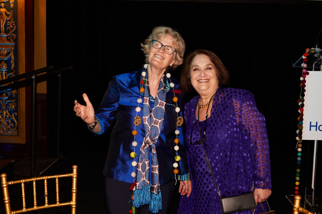 Two women stand side by side both are wearing blue.