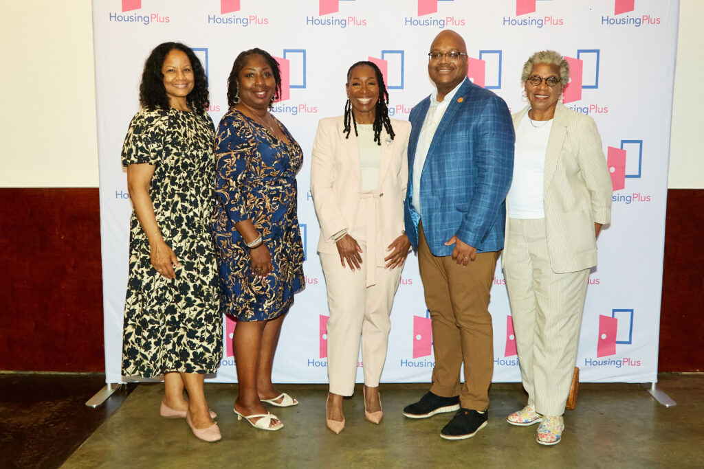 A group of five people in front of step and repeat they are all smiling