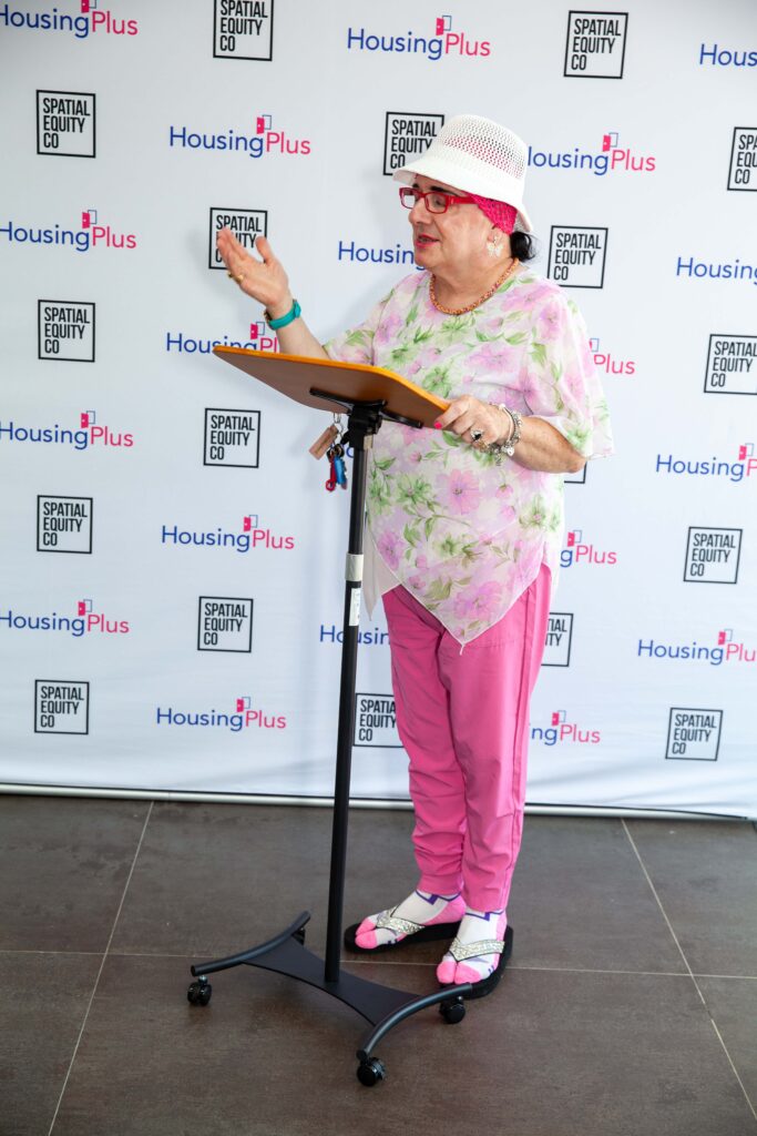 Woman in pink outfit and white hat at podium