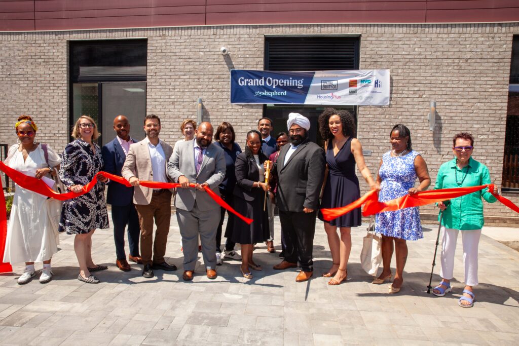 Group of people with a recently cut ribbon in front of supportive housing
